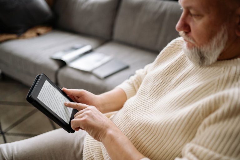 Homme âgé utilisant une tablette pour lire un ebook de psychologie dans un salon confortable et chaleureux.