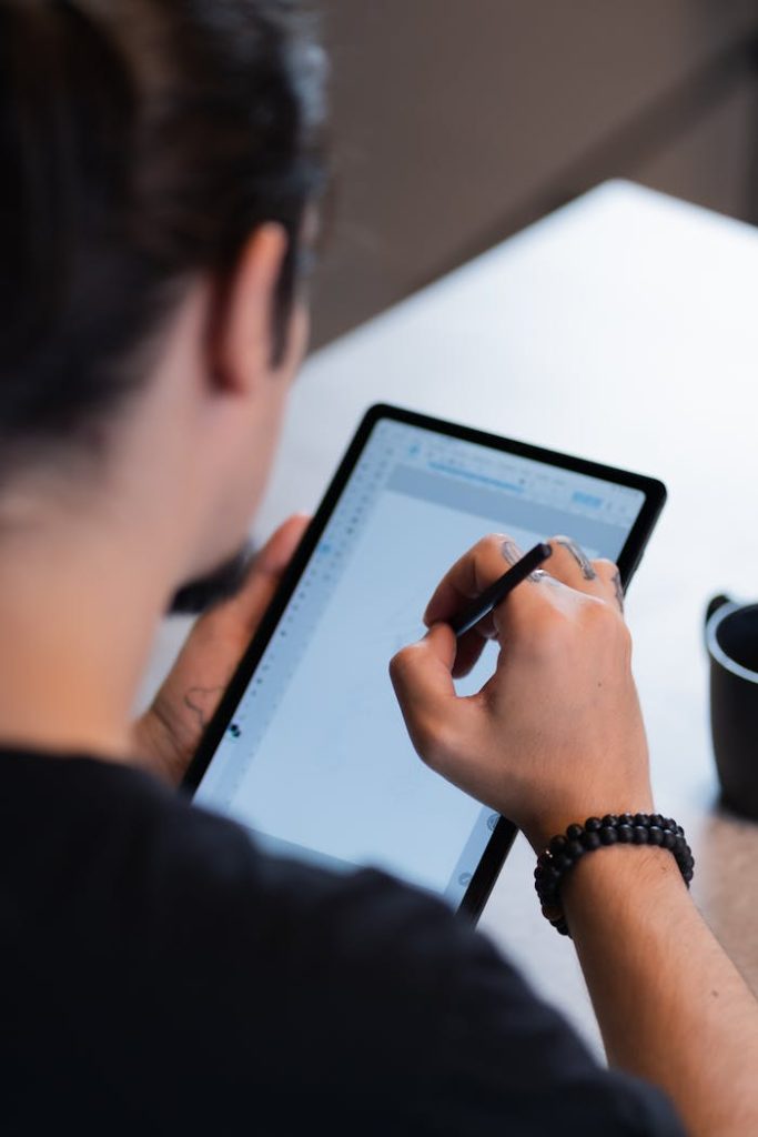 Person using a stylus to draw on a digital tablet, indoors setting.